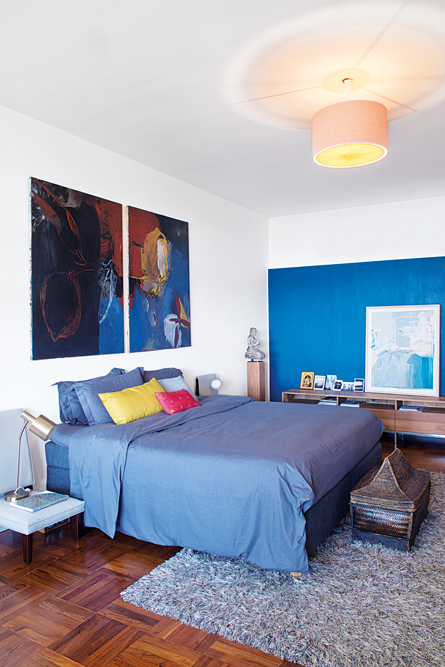 A recently painted royal blue feature wall serves as a perfect backdrop for a painting in the master bedroom; a hand-woven basket shaped like a house sits at the foot of the bed.