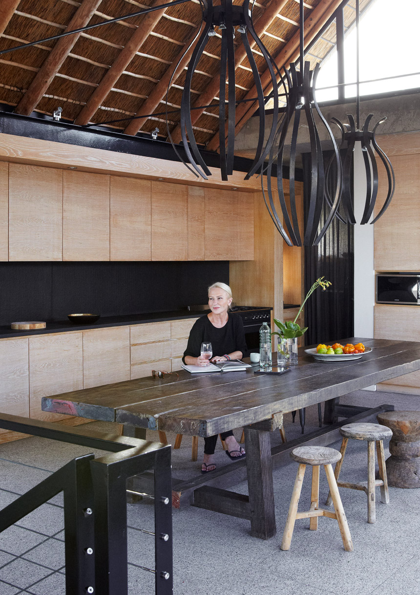 Liz sits at the enormous rustic James Mudge table in the upper living level, which has been treated as one large space, with the kitchen as its hub.
