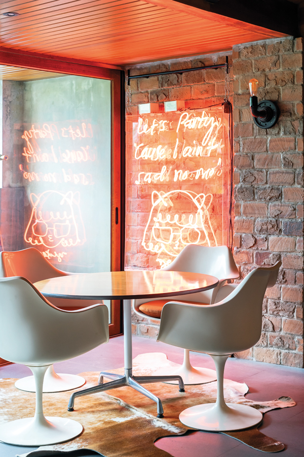 Eero Saarinen’s Tulip chairs surround a table under a neon work by Filipino artist Yeo Kaa, entitled Let’s Party ‘Cause I Ain’t Sad No More