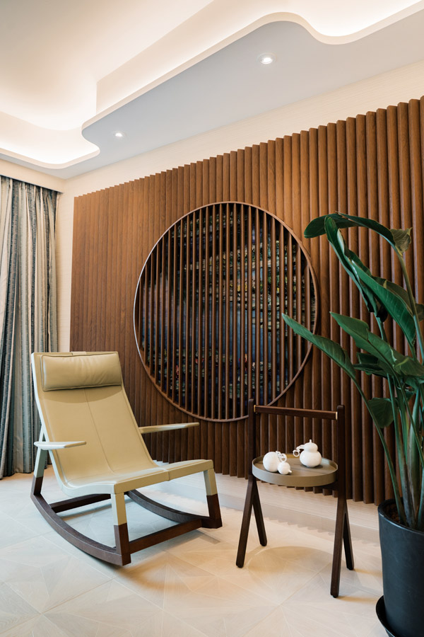 A rocking armchair, teaware and foliage sit against the beautiful dark wooden slat wall underneath which a mural rendition of Monet’s Water Lilies peeks through