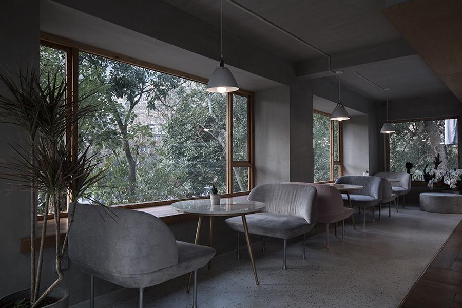 Large bay windows invite more of the outdoors into the cafe's indoor space, furnished with homely grey and mauve seating, amidst bright wood detail. (Photo: UNITU, courtesy of PROJECT Architects)