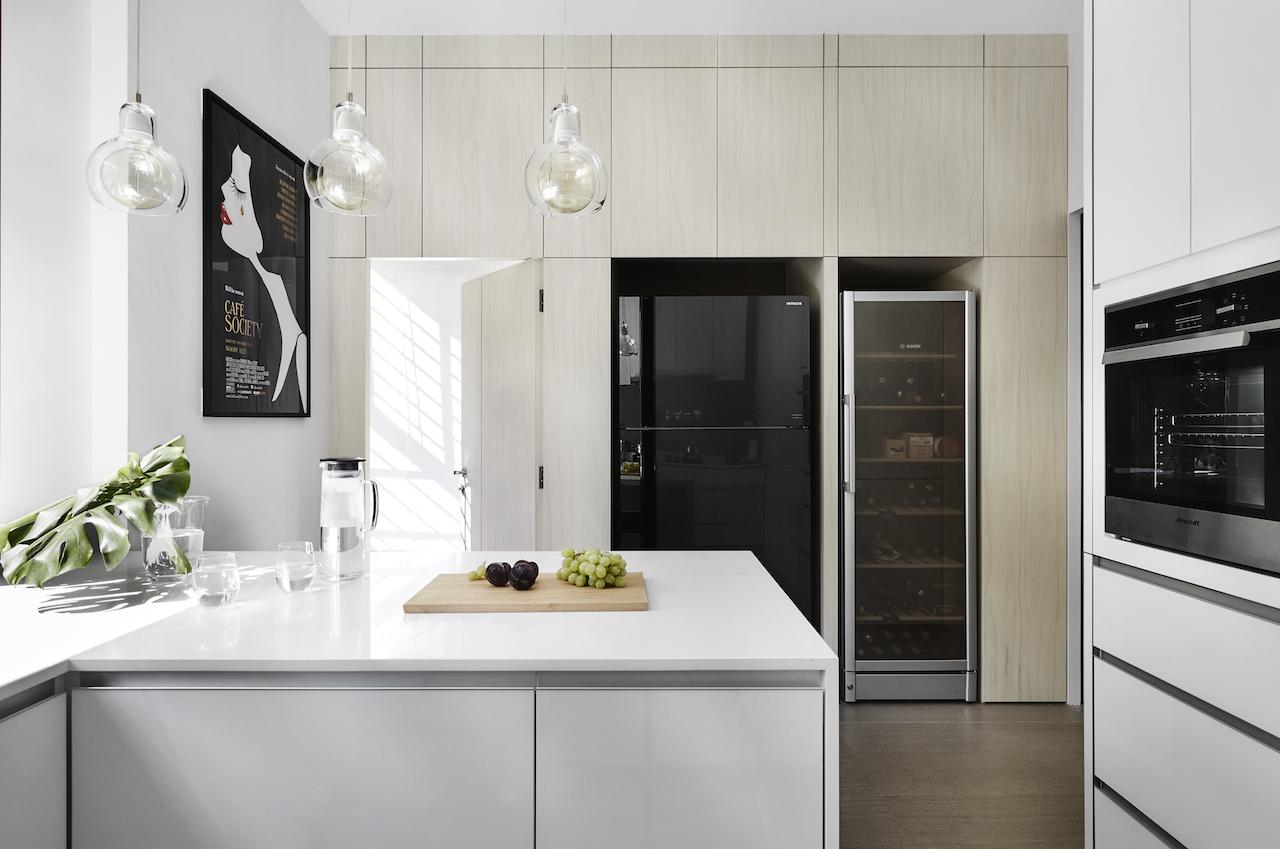 Often drenched in light, the kitchen features neutral-coloured panelling, polished white counters, and neatly built-in appliances.