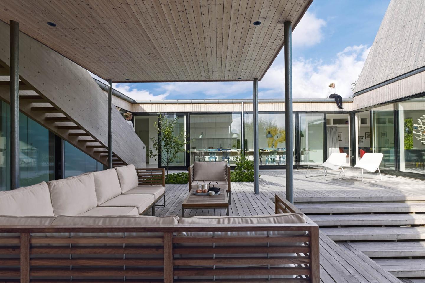 Slender steel columns support an overhang to create a sheltered external living area with locally designed sofas by Salt Trädgårdmöbler