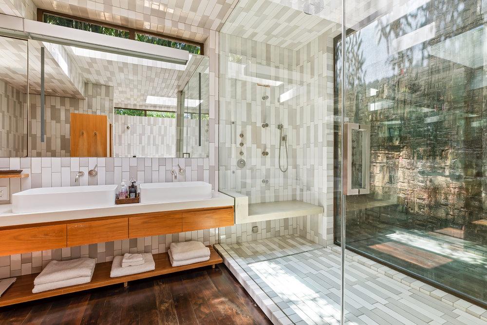 Outfitted in ceramic tiles, the master bathroom boasts views of a water-wall sculpture by Stan Bitters