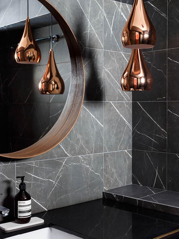 浴室以深色大理石材作牆飾，再加上同色系的圓框木鏡、銅吊燈，美學主題一致連貫